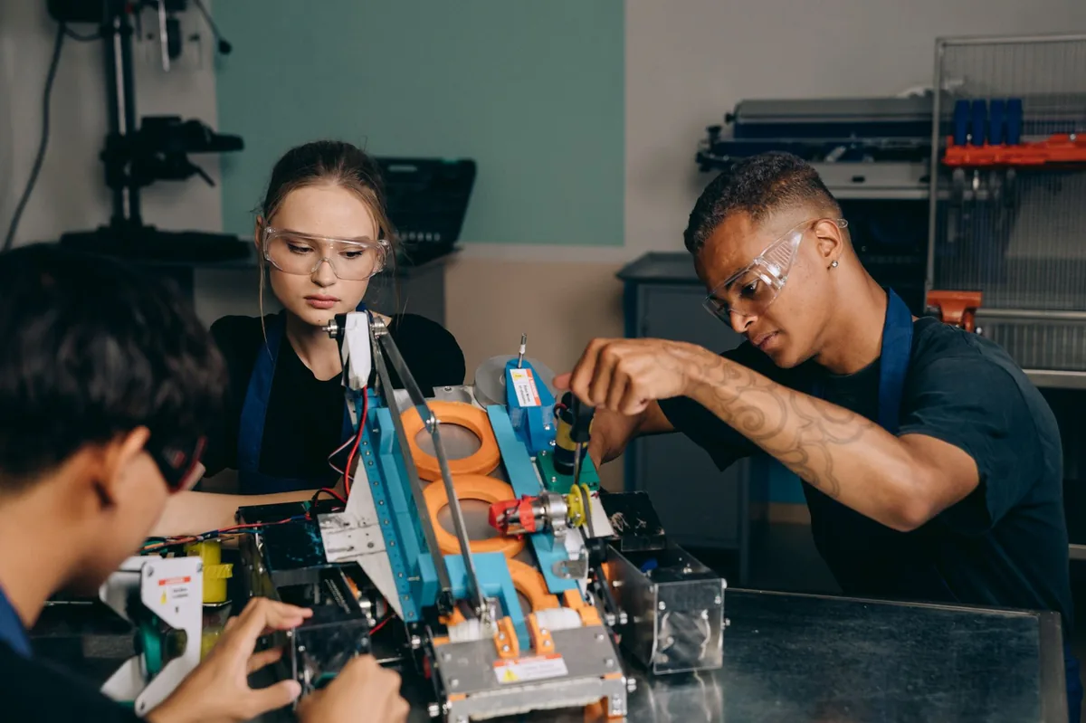 Students in safety glasses wiring and testing a robotic mechanism