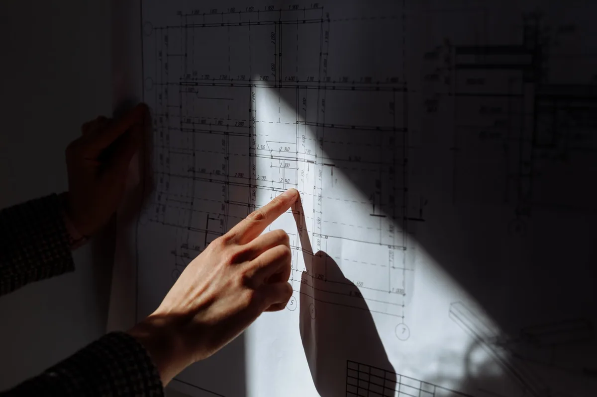 Hand pointing at a technical drawing under directional light