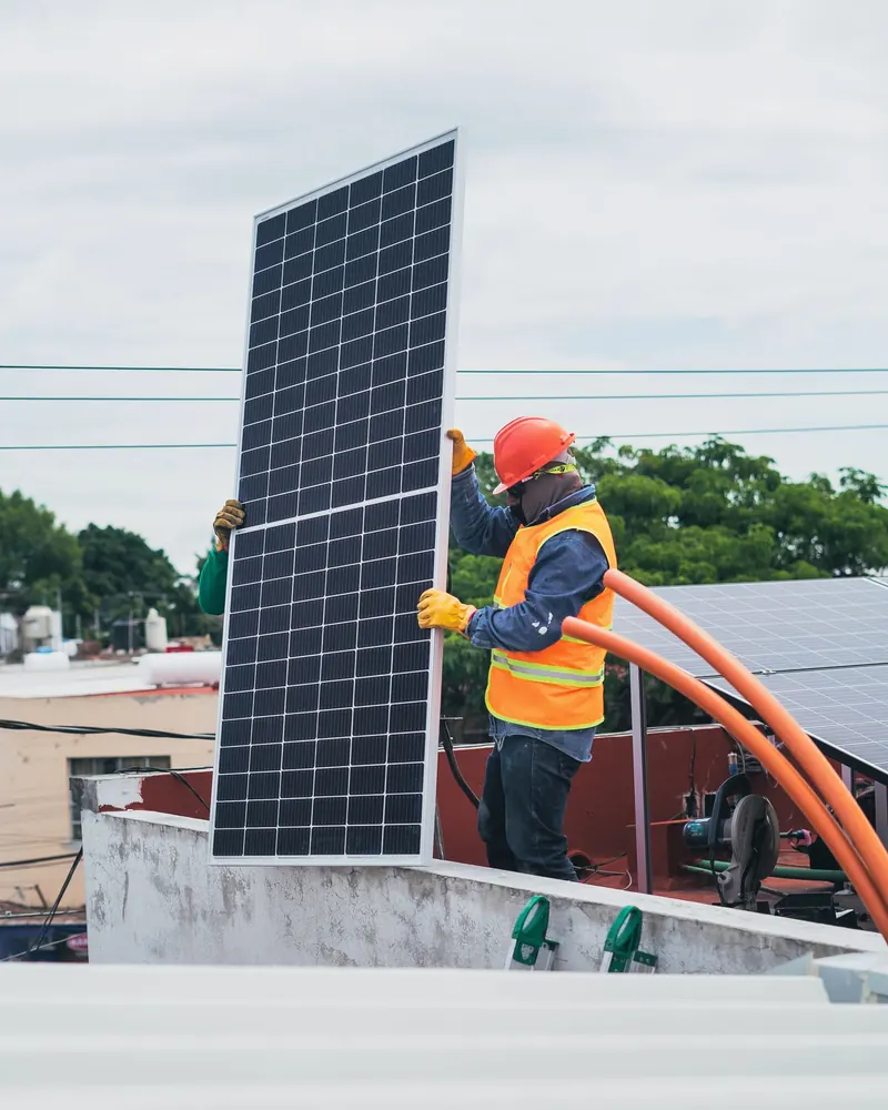 Technician carrying a solar panel across a flat concrete rooftop during a solar installation